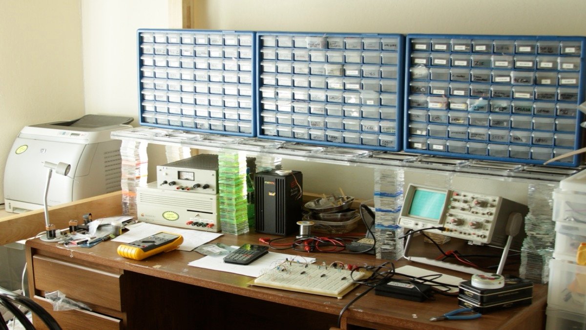 Electronics maker workbench equipped with soldering station, digital multimeter, circuit boards, and electronic test components