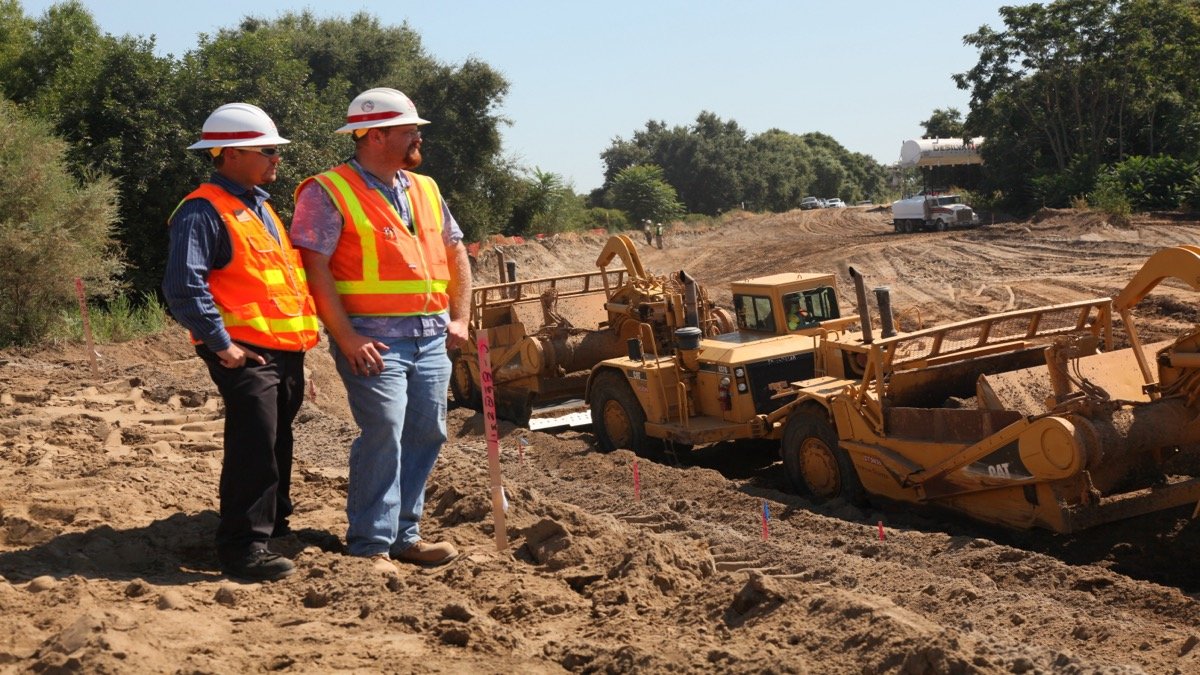 Heavy civil engineering excavators and earthmoving machinery building and fortifying a reinforced flood levee barrier
