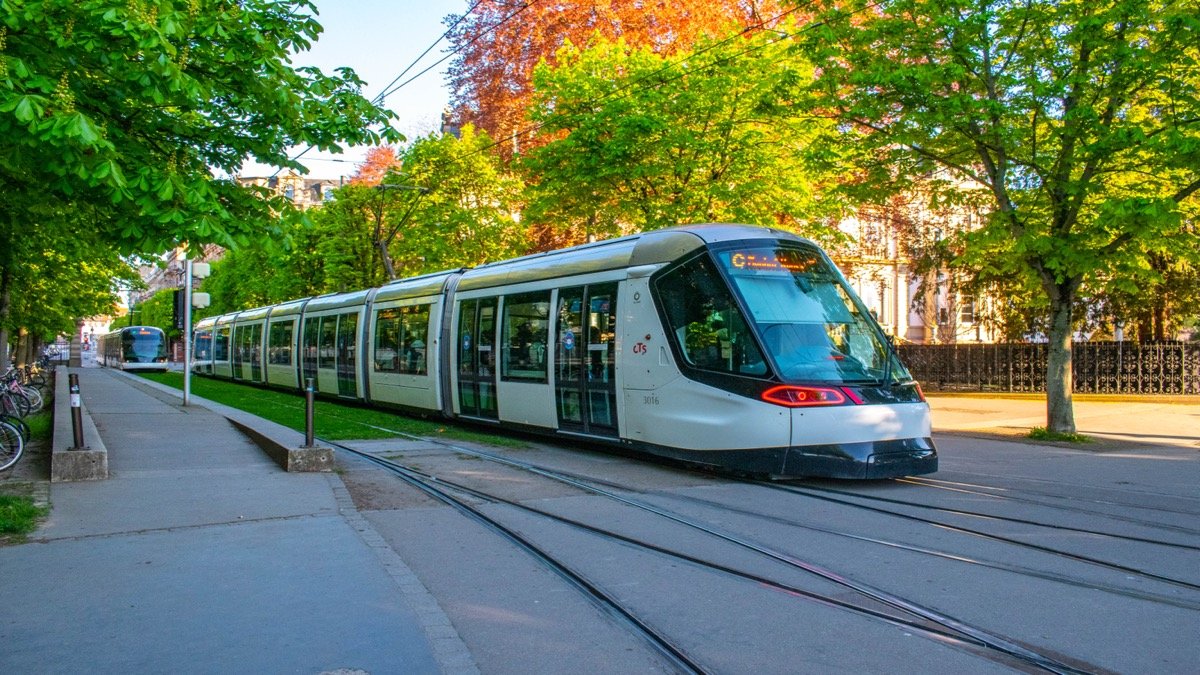 Modern clean electric passenger tram gliding smoothly along a green civic square and tree-lined street in a European city