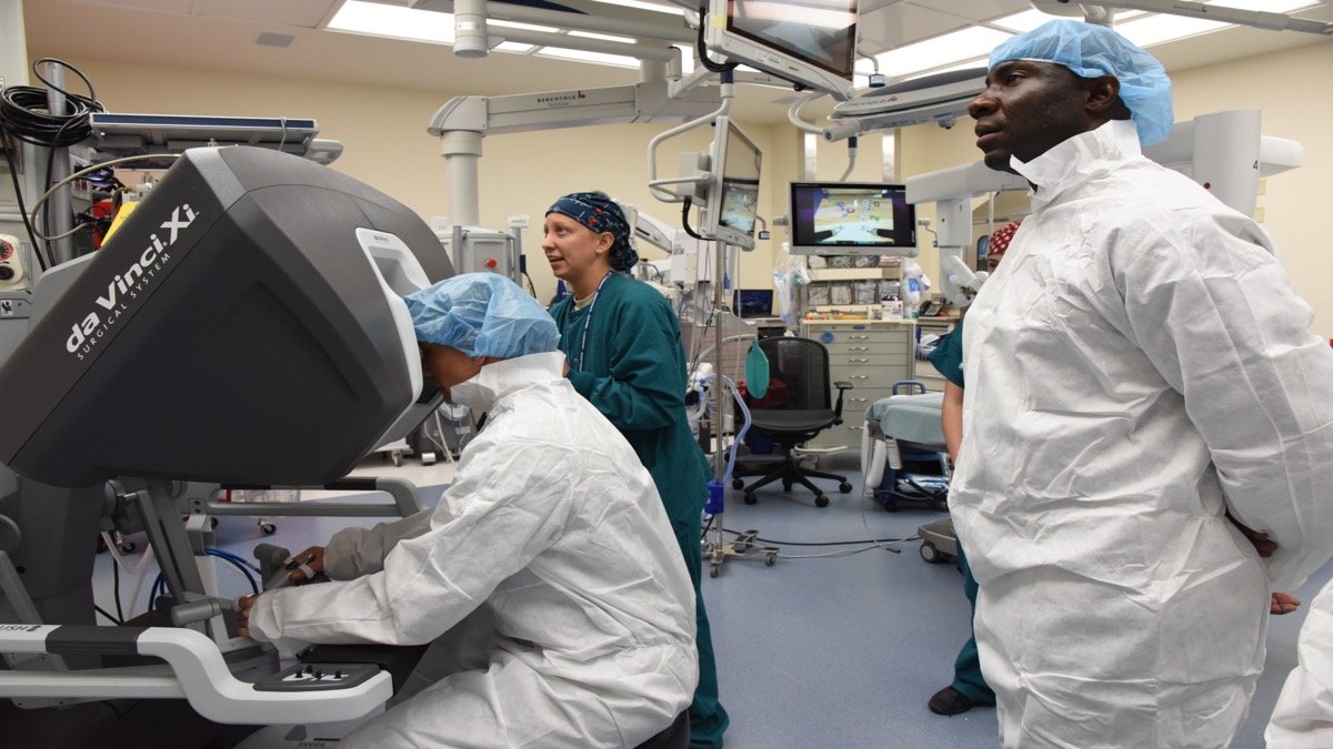 Surgical operating team maneuvering precision robotic surgery controls and high-definition clinical displays in a sterile operating theater