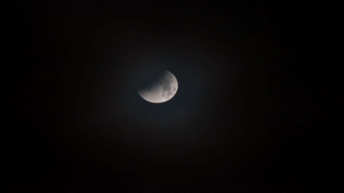 Harvest supermoon rising in night sky with partial lunar eclipse shadow