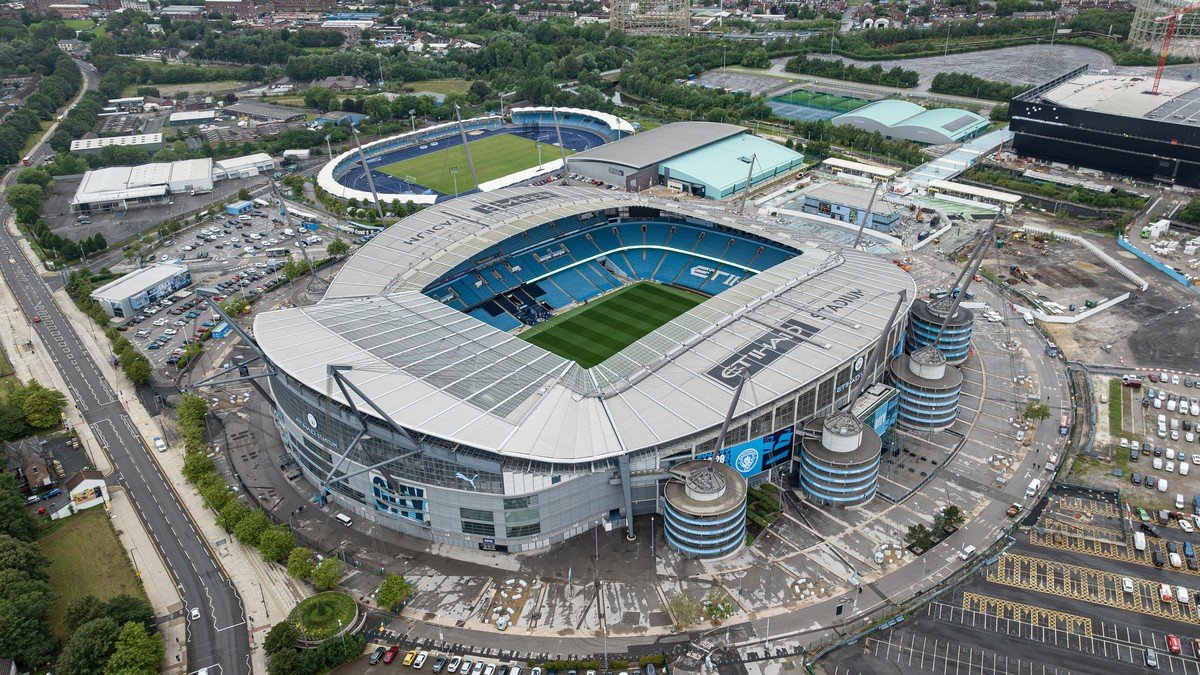 Pep Guardiola speaking at a press conference at the Etihad Stadium with Manchester City crest in background