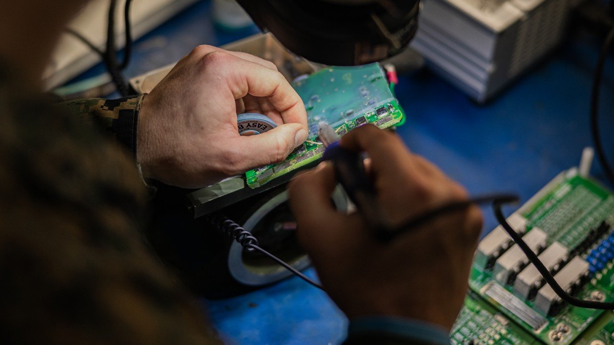 A technician repairing a disassembled smartphone on a workbench with electronic tools and display screens