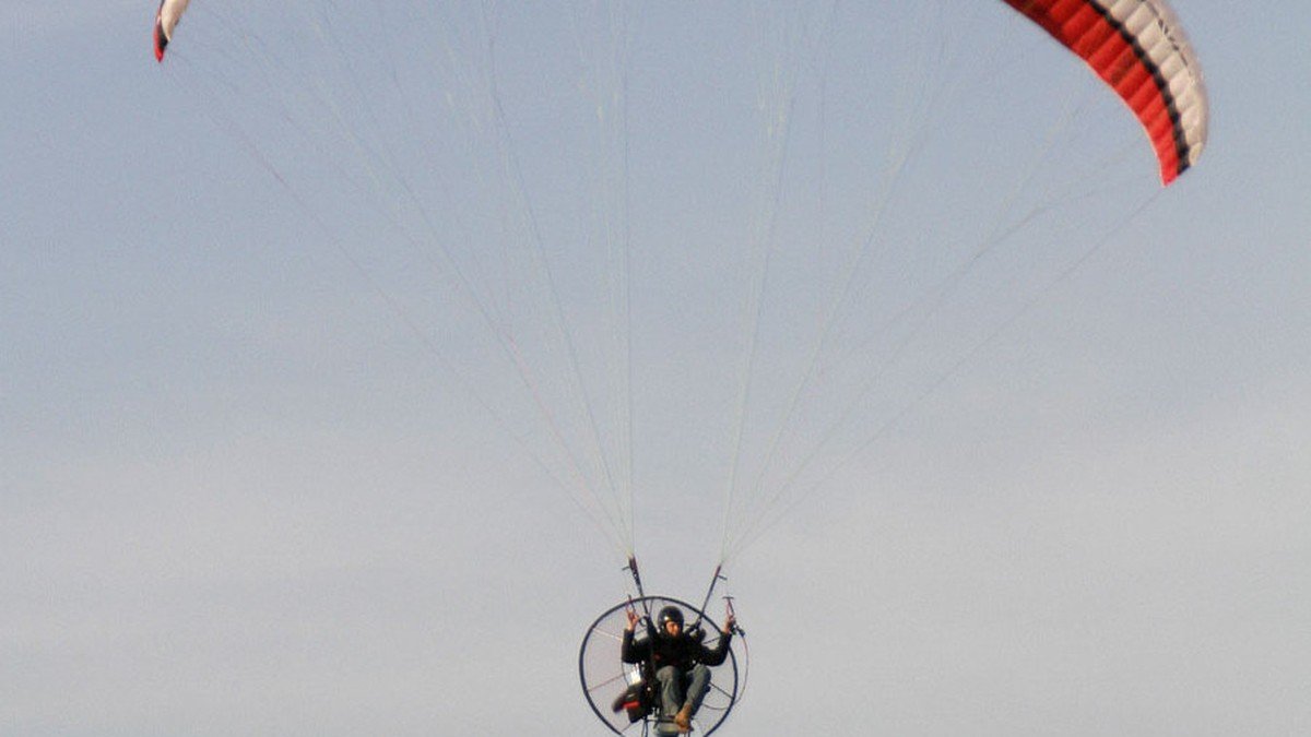Electric paramotor pilot soaring above calm coastal waters during sunrise over the Strait of Malacca